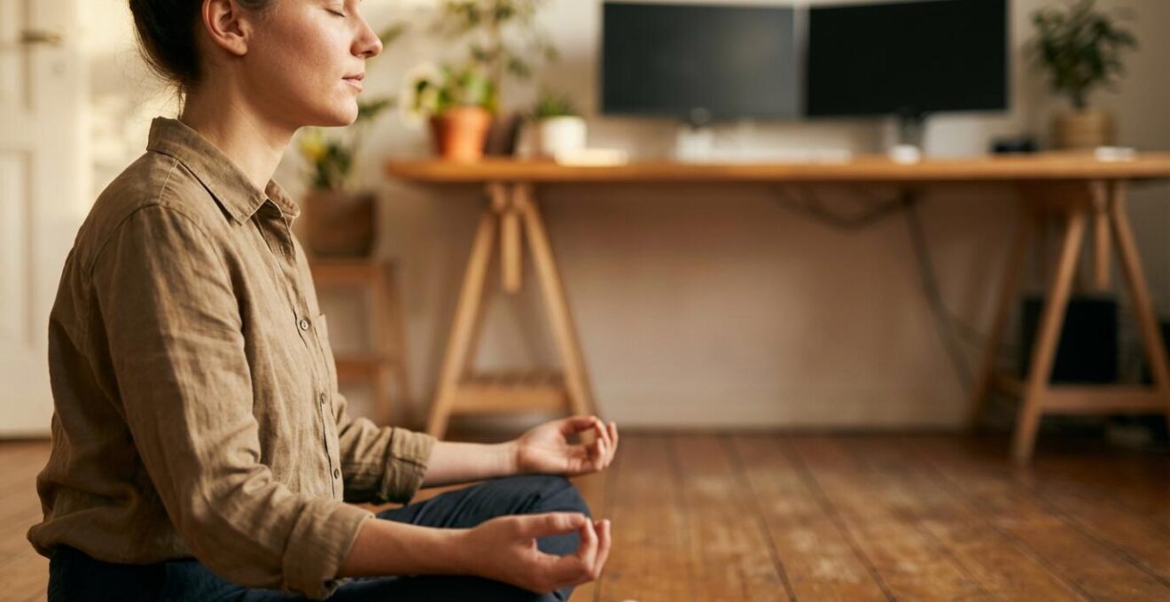 Person practicing meditation in home office with trading setup in background